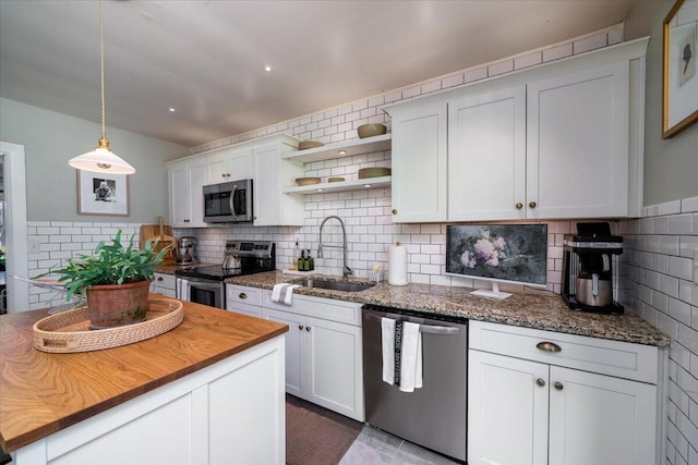 kitchen featuring wood counters, decorative light fixtures, stainless steel appliances, white cabinetry, and a sink