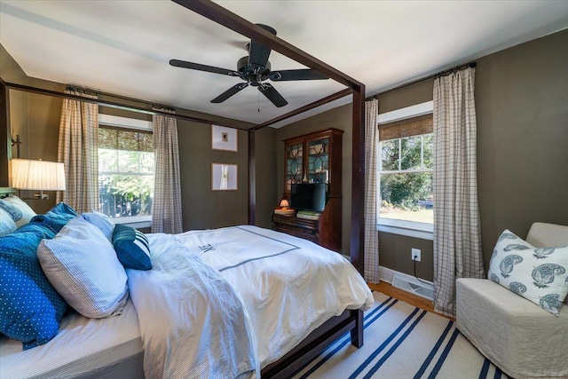 bedroom with a ceiling fan, multiple windows, baseboards, and wood finished floors