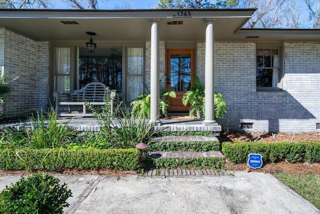 entrance to property with covered porch, brick siding, and crawl space