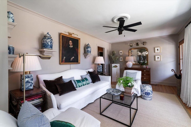 living room featuring ornamental molding, baseboards, ceiling fan, and light wood finished floors