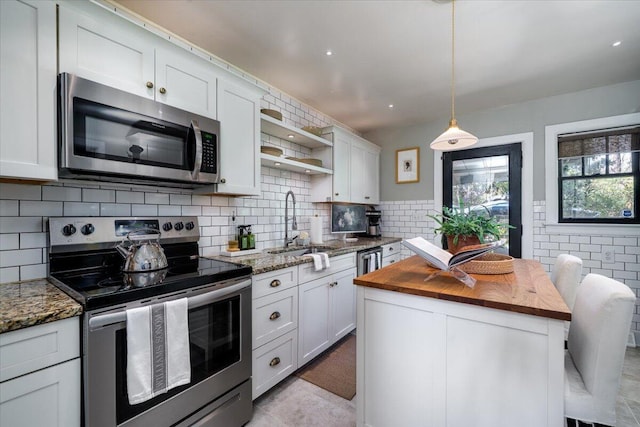 kitchen with hanging light fixtures, appliances with stainless steel finishes, white cabinetry, a kitchen island, and dark stone countertops