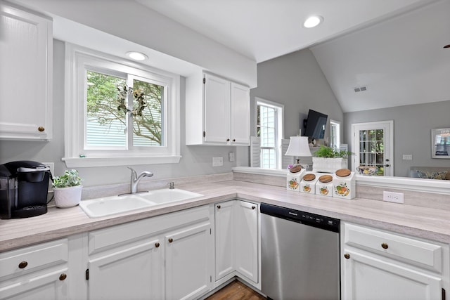 kitchen with stainless steel dishwasher, a sink, healthy amount of natural light, lofted ceiling, and white cabinets