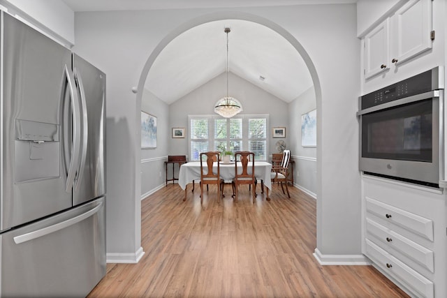 dining space featuring arched walkways, baseboards, light wood-style floors, and vaulted ceiling