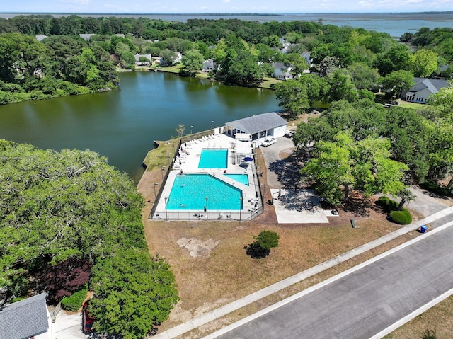 bird's eye view of a pool area, a large body of water, and a tree filled landscape