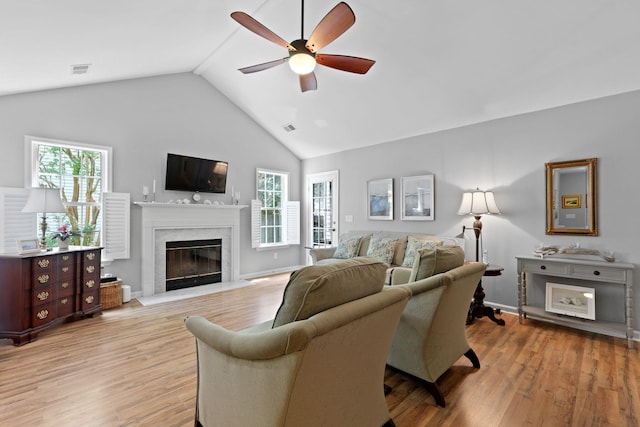 living room with a ceiling fan, a fireplace, light wood-style flooring, high vaulted ceiling, and baseboards