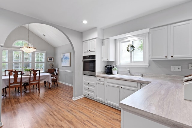 kitchen featuring stainless steel oven, a sink, light countertops, vaulted ceiling, and arched walkways