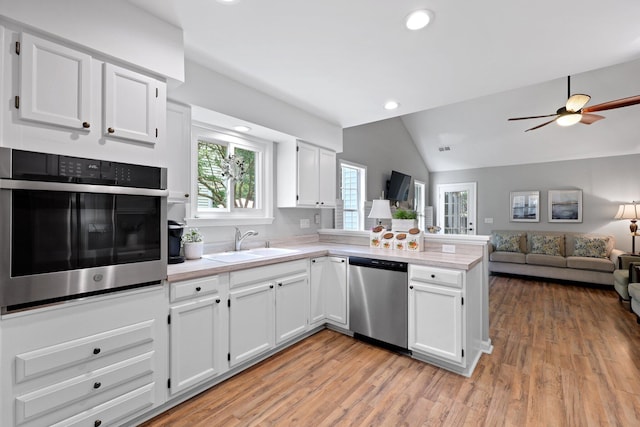 kitchen featuring appliances with stainless steel finishes, a sink, a peninsula, vaulted ceiling, and light countertops