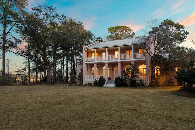 back house at dusk with a balcony, a yard, and covered porch