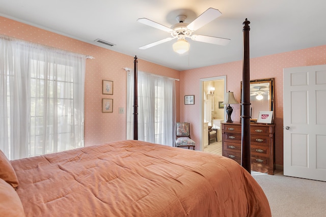 bedroom with ensuite bath, multiple windows, ceiling fan, and light colored carpet