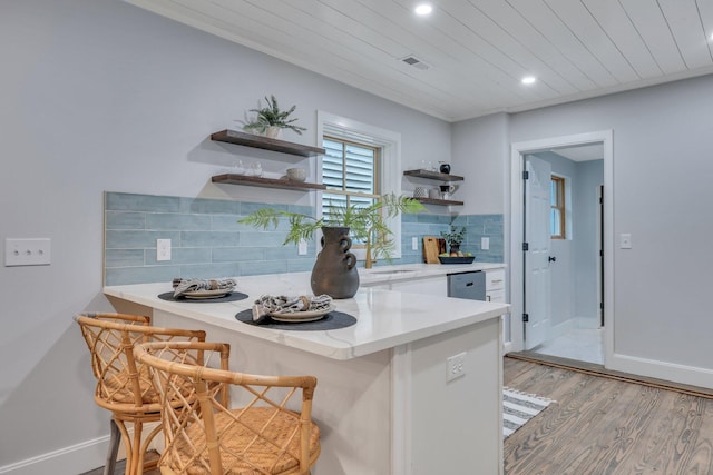 kitchen featuring a breakfast bar area, tasteful backsplash, wood ceiling, light wood-type flooring, and kitchen peninsula