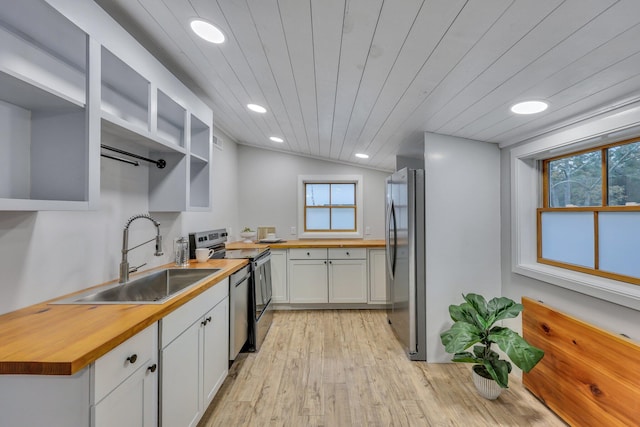 kitchen with lofted ceiling, sink, butcher block countertops, white cabinetry, and appliances with stainless steel finishes