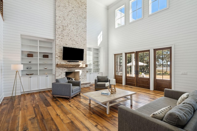 living room featuring a fireplace, dark hardwood / wood-style flooring, built in shelves, a high ceiling, and french doors