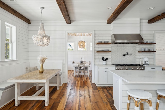 kitchen with decorative light fixtures, a notable chandelier, a kitchen bar, white cabinets, and wall chimney exhaust hood