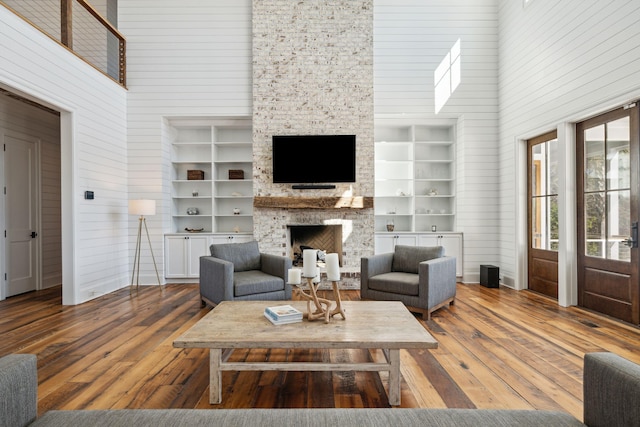 living room with a high ceiling, built in shelves, dark hardwood / wood-style flooring, and a fireplace