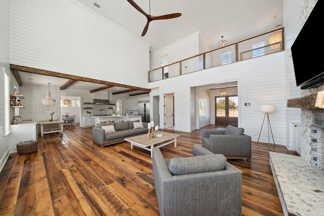 living room with ceiling fan, beam ceiling, a fireplace, a towering ceiling, and dark hardwood / wood-style floors