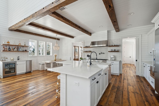 kitchen with a kitchen breakfast bar, white cabinets, fume extractor, a center island with sink, and beverage cooler