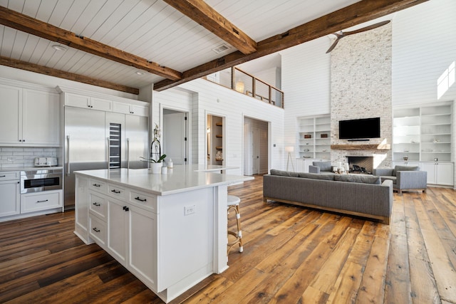 kitchen with dark hardwood / wood-style flooring, white cabinets, beamed ceiling, a stone fireplace, and a center island