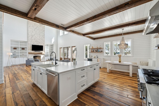 kitchen with decorative light fixtures, dark hardwood / wood-style floors, a fireplace, a kitchen island with sink, and white cabinets