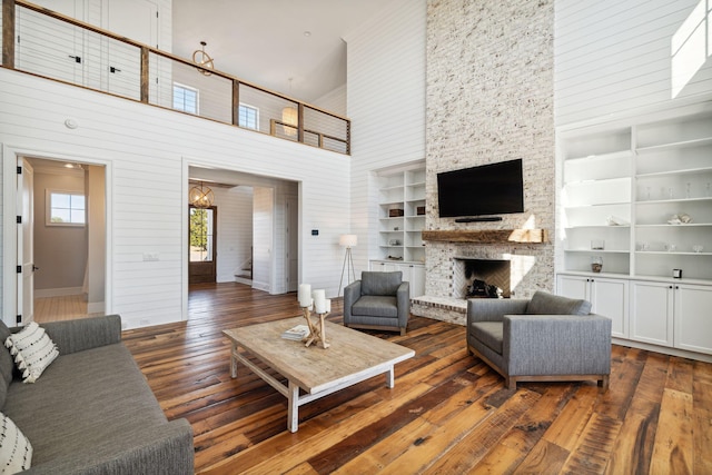 living room featuring dark hardwood / wood-style flooring, an inviting chandelier, a stone fireplace, built in features, and a high ceiling