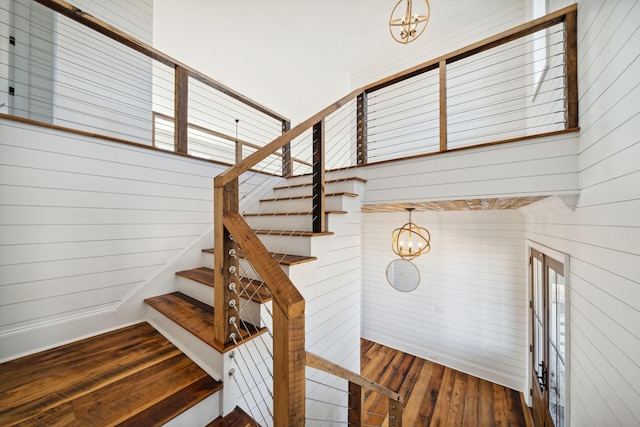 staircase with wood walls, dark hardwood / wood-style floors, and a chandelier