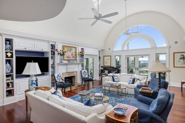 living room with ceiling fan, a towering ceiling, built in shelves, dark hardwood / wood-style floors, and french doors