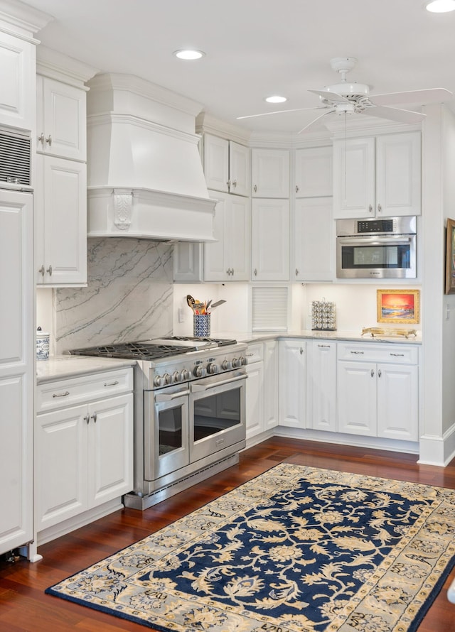 kitchen with appliances with stainless steel finishes, ceiling fan, white cabinetry, custom exhaust hood, and backsplash