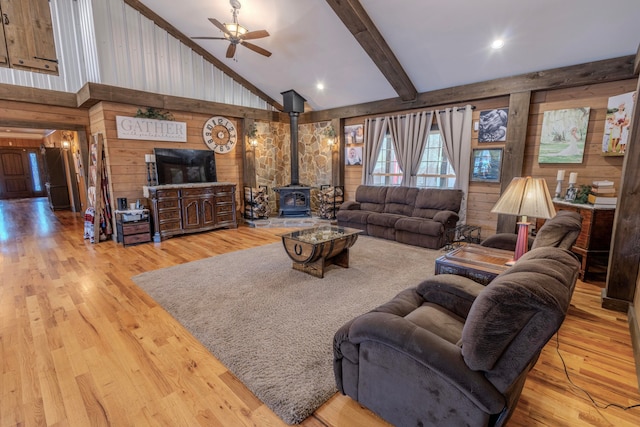 living room featuring wood walls, ceiling fan, a wood stove, and light hardwood / wood-style flooring