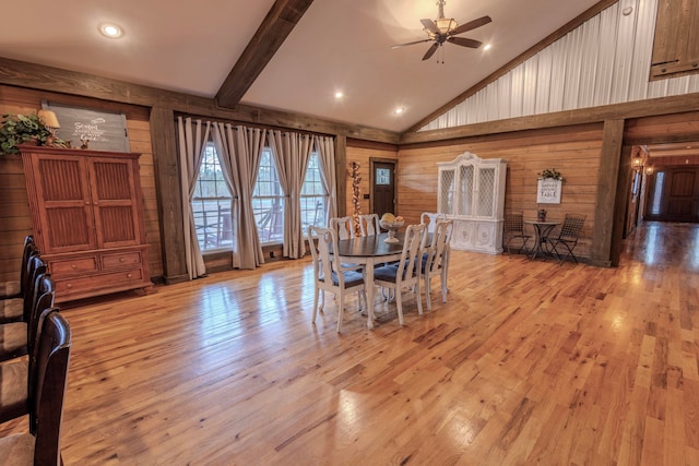 dining room featuring light wood-type flooring, beamed ceiling, ceiling fan, wood walls, and high vaulted ceiling