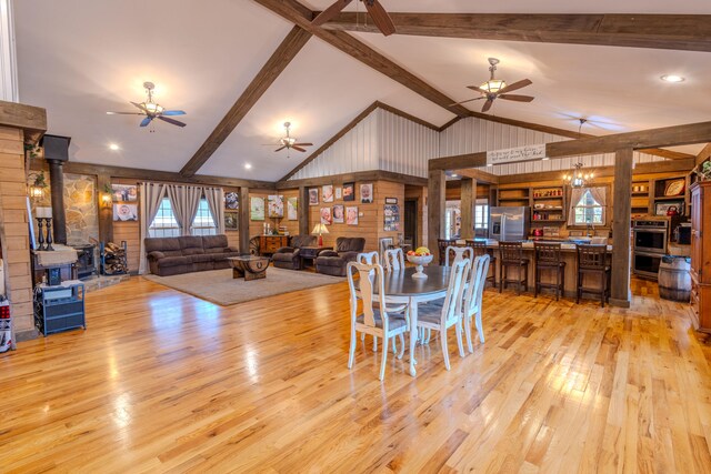 dining area with wooden walls, a wood stove, light hardwood / wood-style floors, and ceiling fan with notable chandelier