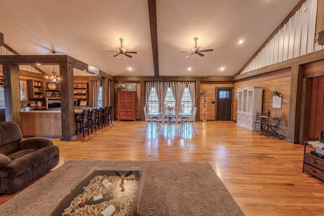 living room with wooden walls, light hardwood / wood-style floors, vaulted ceiling with beams, and ceiling fan with notable chandelier