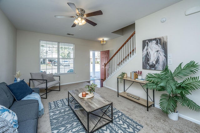 carpeted living area with stairs, ceiling fan, visible vents, and baseboards