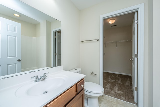 bathroom featuring a walk in closet, vanity, toilet, and tile patterned floors