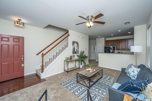 living room with dark colored carpet, visible vents, stairway, a ceiling fan, and baseboards