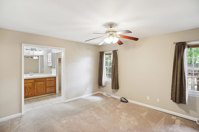 unfurnished bedroom with light tile patterned flooring, ensuite bathroom, sink, and ceiling fan