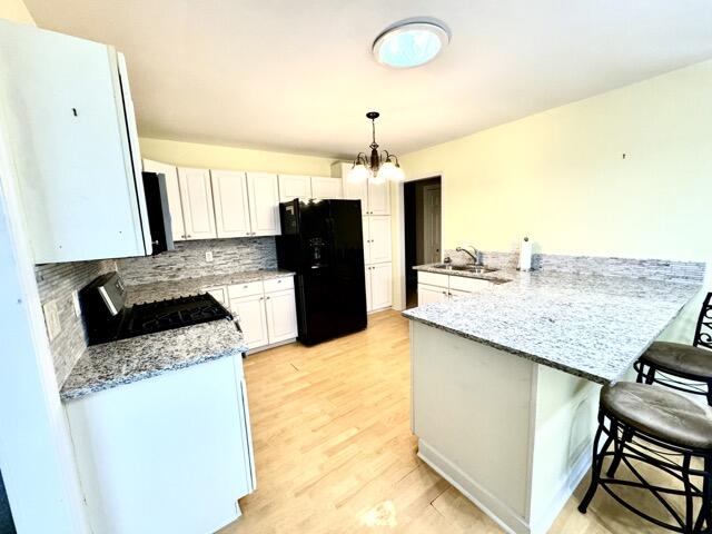 kitchen with kitchen peninsula, backsplash, black refrigerator, light hardwood / wood-style floors, and stove