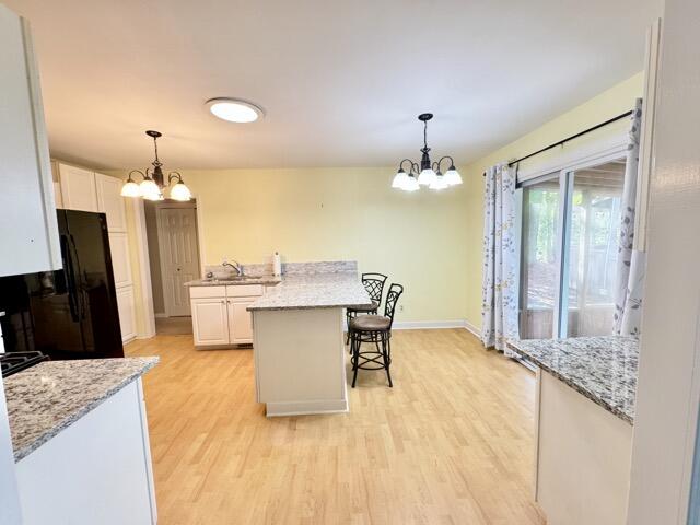 kitchen with light hardwood / wood-style flooring, an inviting chandelier, white cabinets, black fridge, and decorative light fixtures