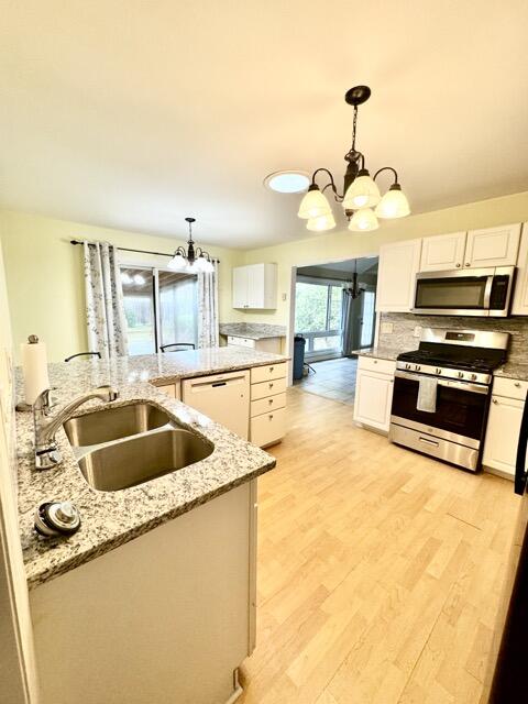 kitchen with light wood-type flooring, white cabinets, stainless steel appliances, decorative backsplash, and sink