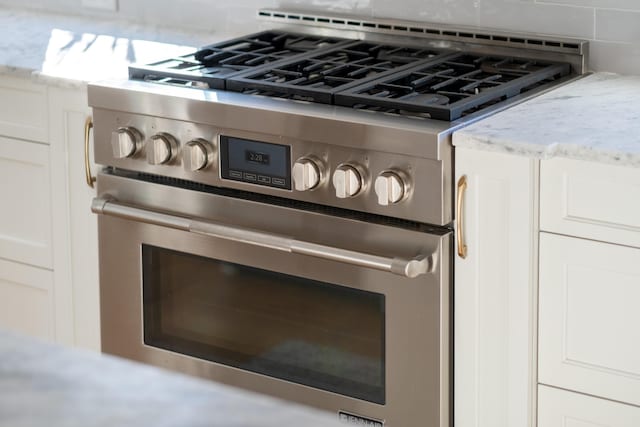 room details featuring white cabinets, light stone countertops, stainless steel range, and tasteful backsplash