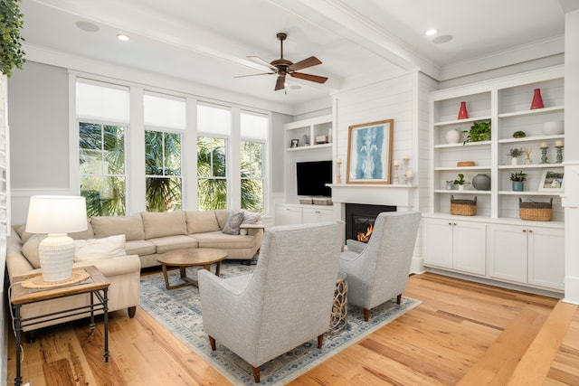 living room with crown molding, ceiling fan, light wood-type flooring, built in features, and beamed ceiling