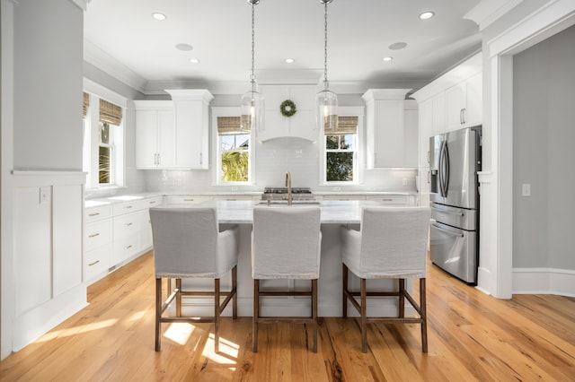 kitchen with white cabinets, stainless steel fridge, an island with sink, and light hardwood / wood-style flooring