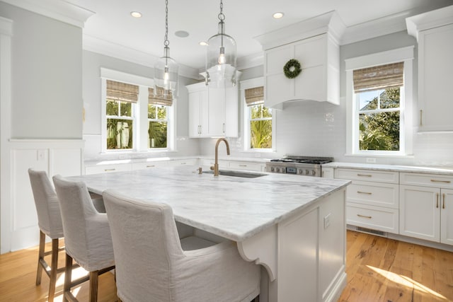 kitchen featuring stove, white cabinetry, an island with sink, and a breakfast bar area