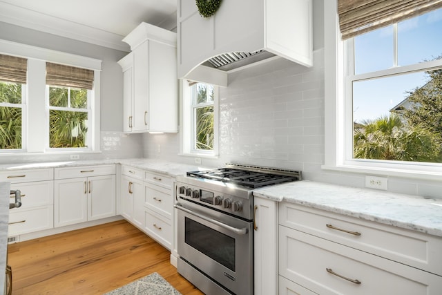 kitchen featuring white cabinetry, light stone countertops, high end stove, backsplash, and extractor fan