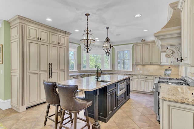 kitchen with cream cabinetry, appliances with stainless steel finishes, decorative light fixtures, and an island with sink