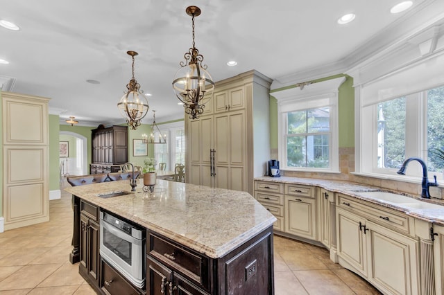 kitchen featuring a kitchen island with sink, cream cabinets, light stone counters, and sink