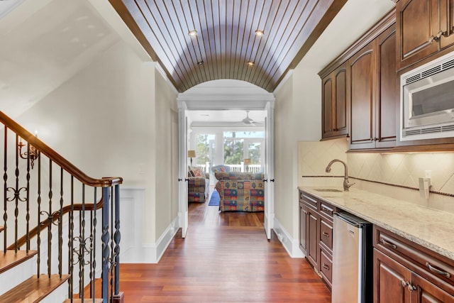 kitchen featuring backsplash, light stone counters, vaulted ceiling, dark hardwood / wood-style floors, and stainless steel microwave