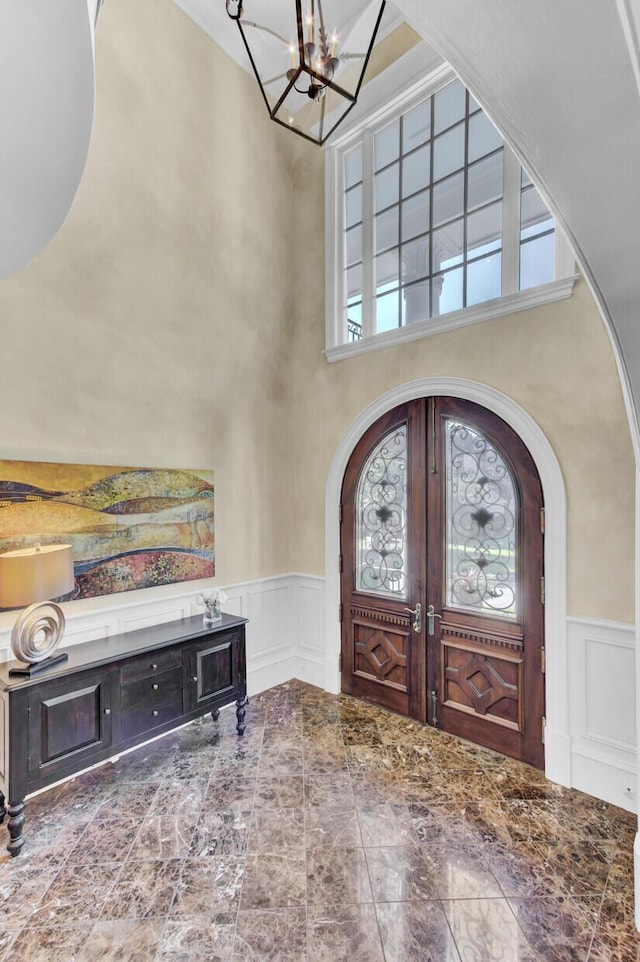 entryway featuring french doors, a towering ceiling, and an inviting chandelier