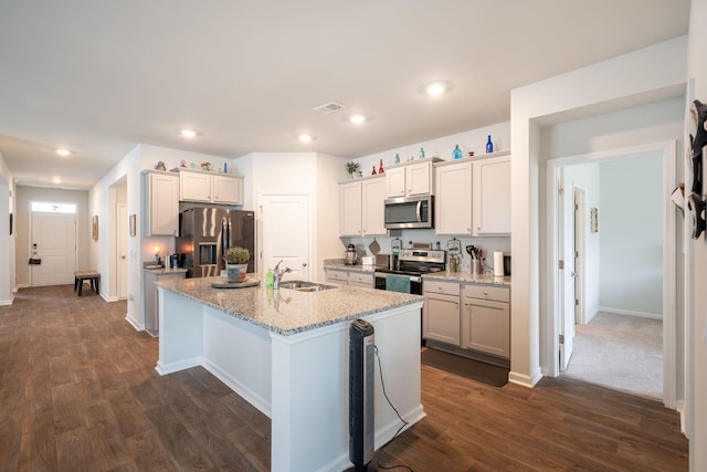 kitchen with light stone countertops, an island with sink, appliances with stainless steel finishes, and dark hardwood / wood-style floors