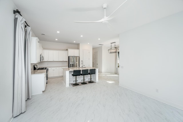 kitchen with a kitchen breakfast bar, ceiling fan, an island with sink, white cabinetry, and stainless steel appliances