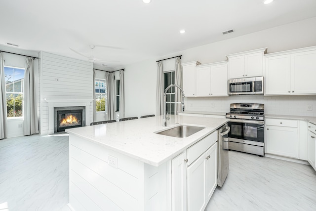 kitchen with backsplash, sink, an island with sink, appliances with stainless steel finishes, and light stone counters