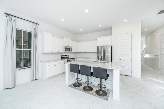 kitchen featuring a breakfast bar, a center island with sink, sink, white cabinetry, and stainless steel appliances